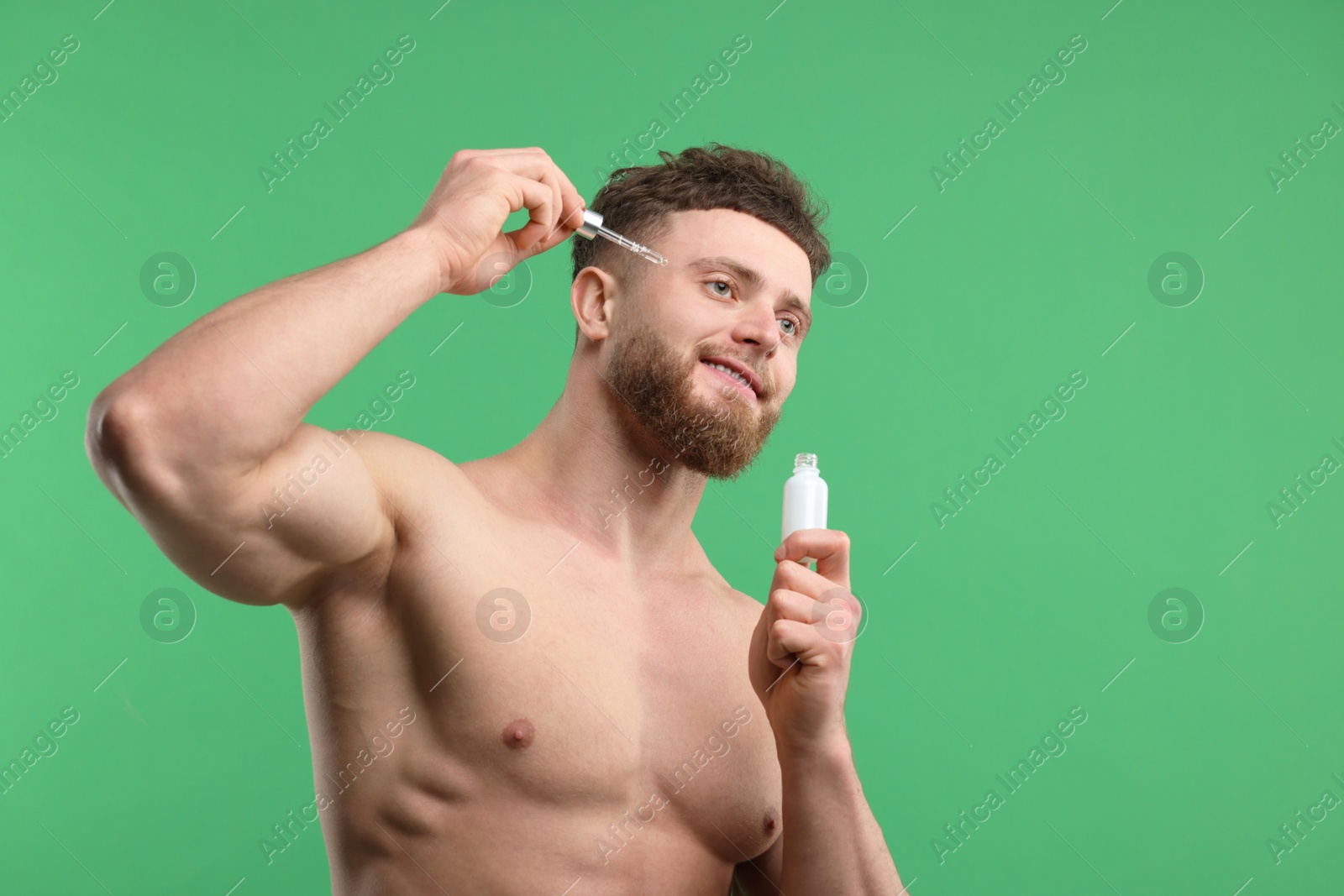 Photo of Handsome man applying serum onto his face on green background, space for text