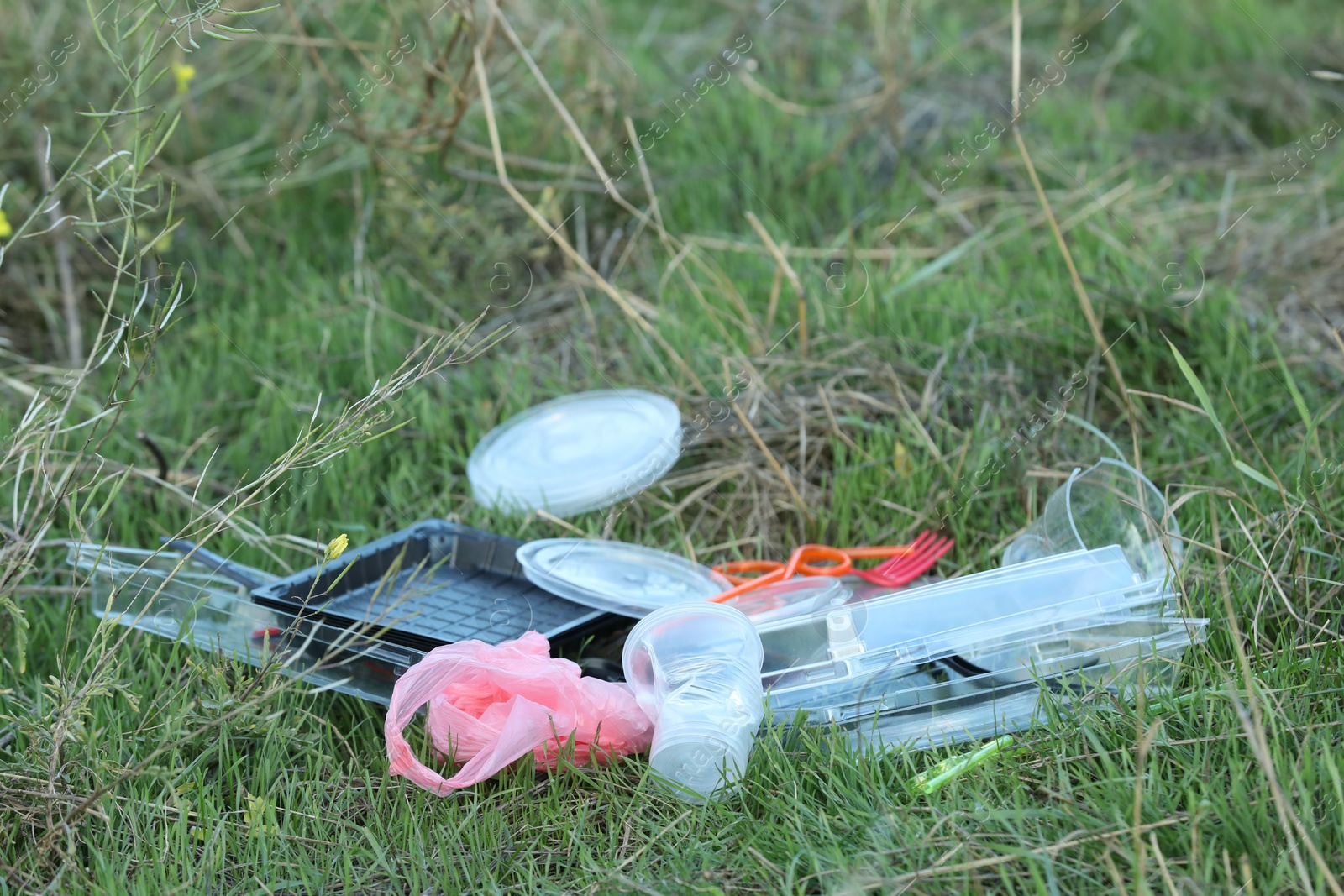 Photo of Used plastic tableware and bag on grass outdoors, space for text. Environmental pollution concept