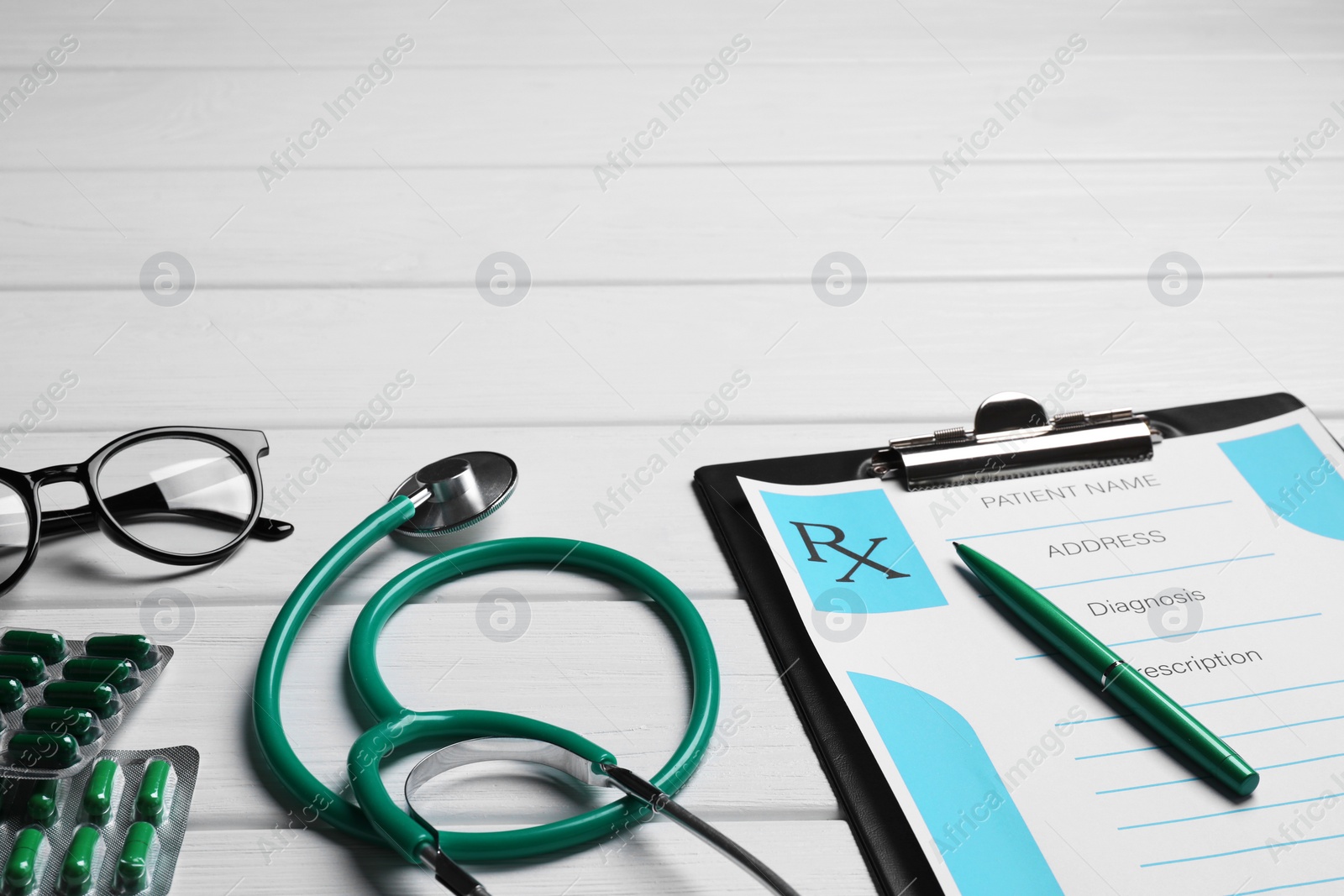 Photo of Clipboard with medical prescription form, stethoscope, pills and glasses on white wooden table. Space for text