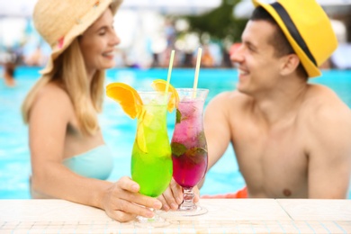 Photo of Happy couple with cocktails resting in blue swimming pool outdoors