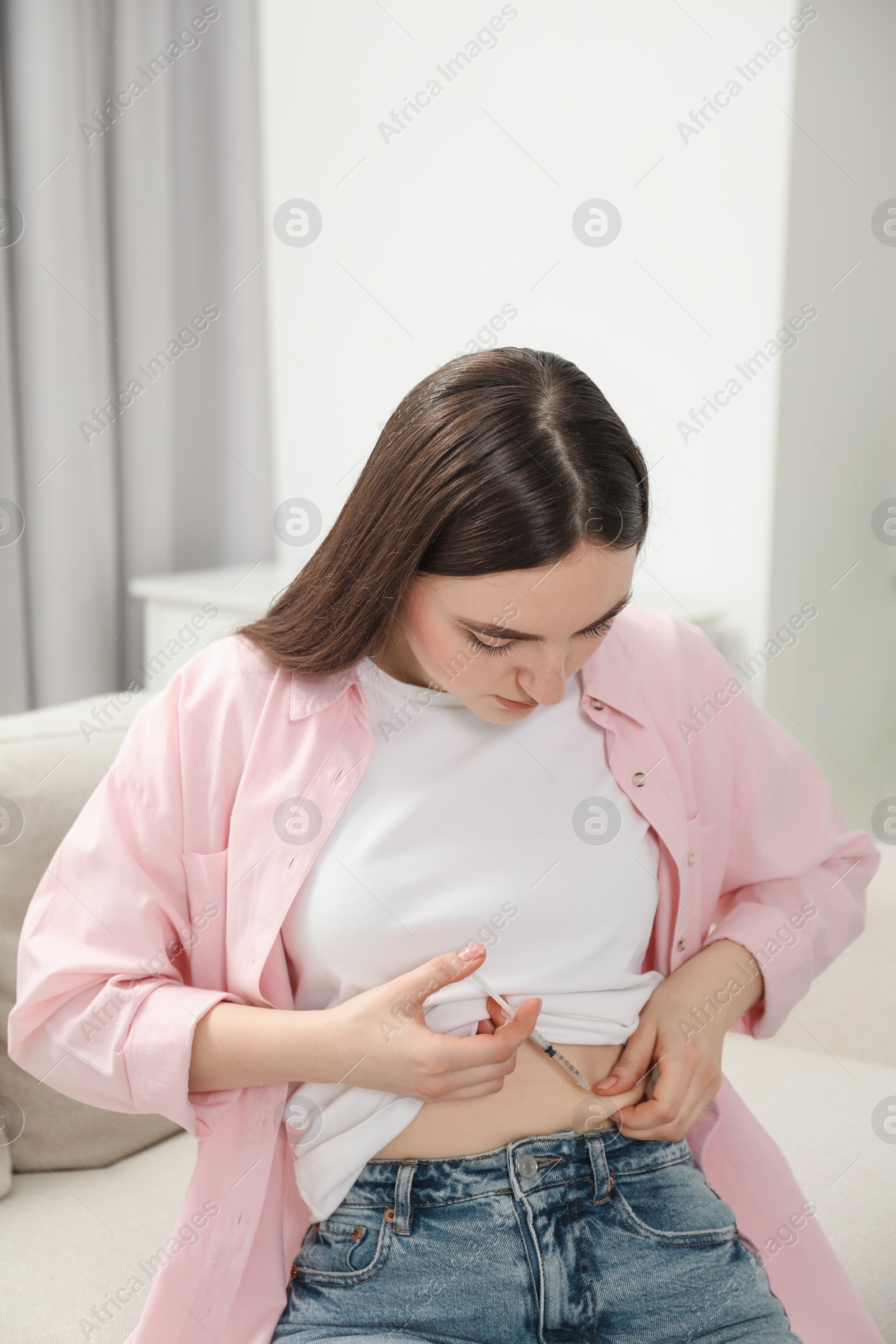 Photo of Diabetes. Woman making insulin injection into her belly on sofa at home