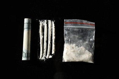 Drug addiction. Plastic bag with cocaine and rolled dollar banknote on black background, flat lay