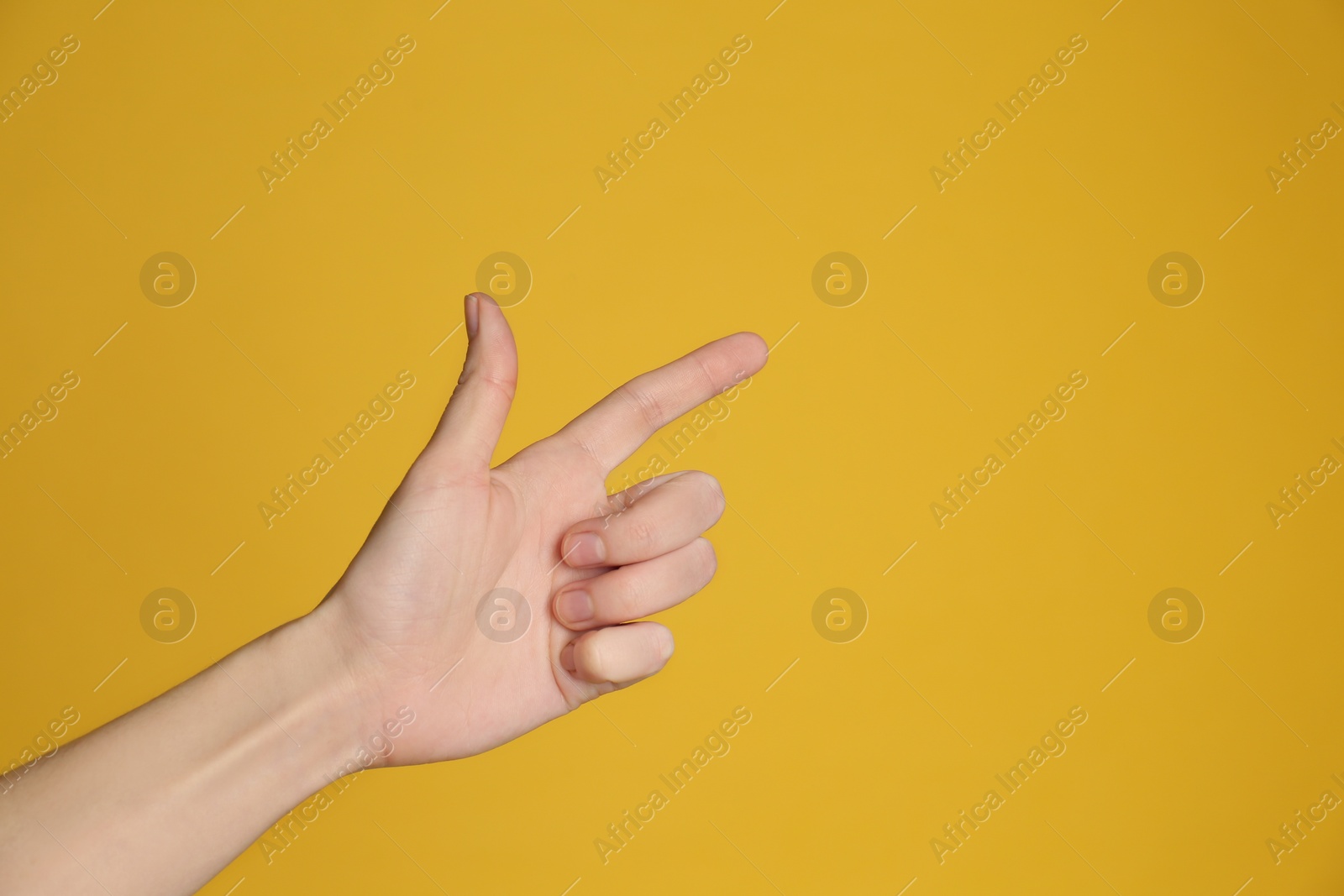 Photo of Woman pointing at something on yellow background, closeup. Finger gesture