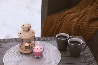 Burning candle, lantern and cups with hot drink on coffee table outdoors. Cosy winter