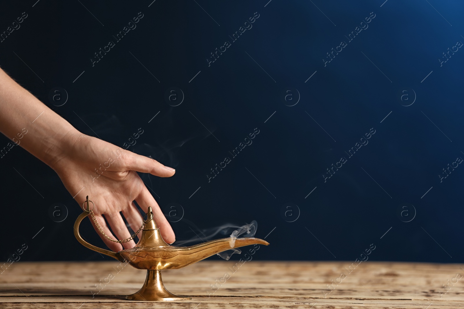 Photo of Woman rubbing magical Aladdin lamp on table against dark background