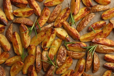 Tasty baked potato and aromatic rosemary on parchment paper, flat lay