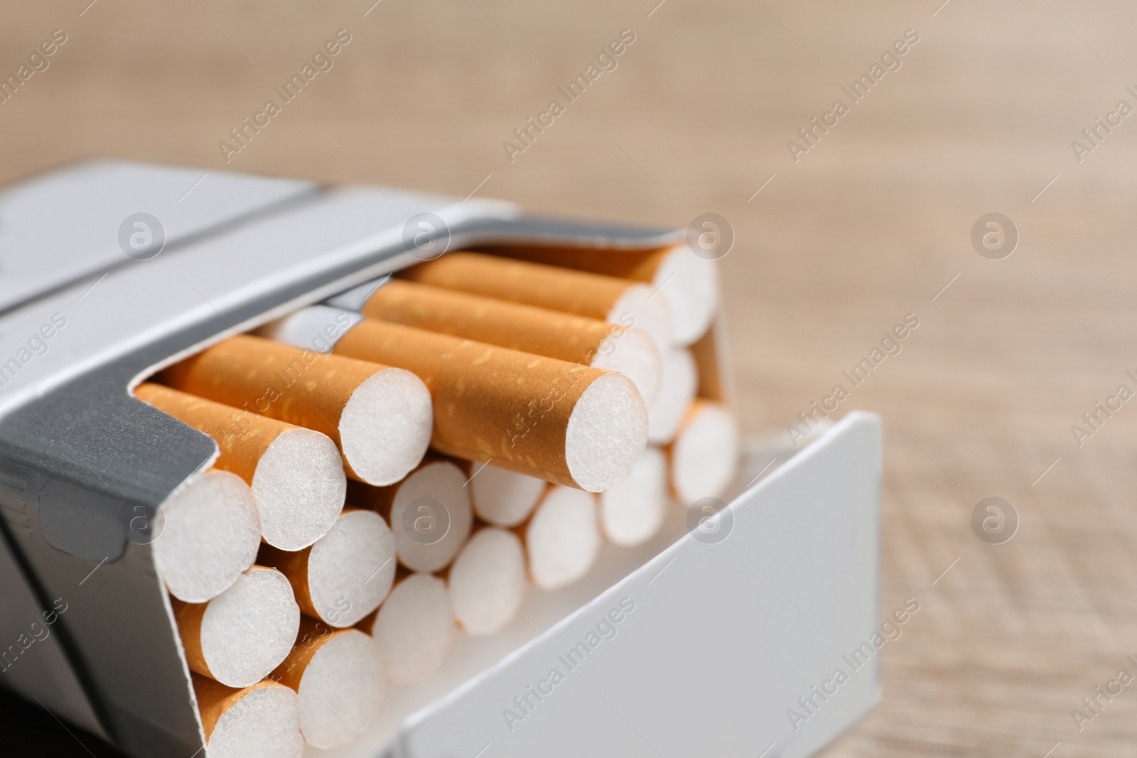 Photo of Cigarettes with orange filters in pack on table, closeup