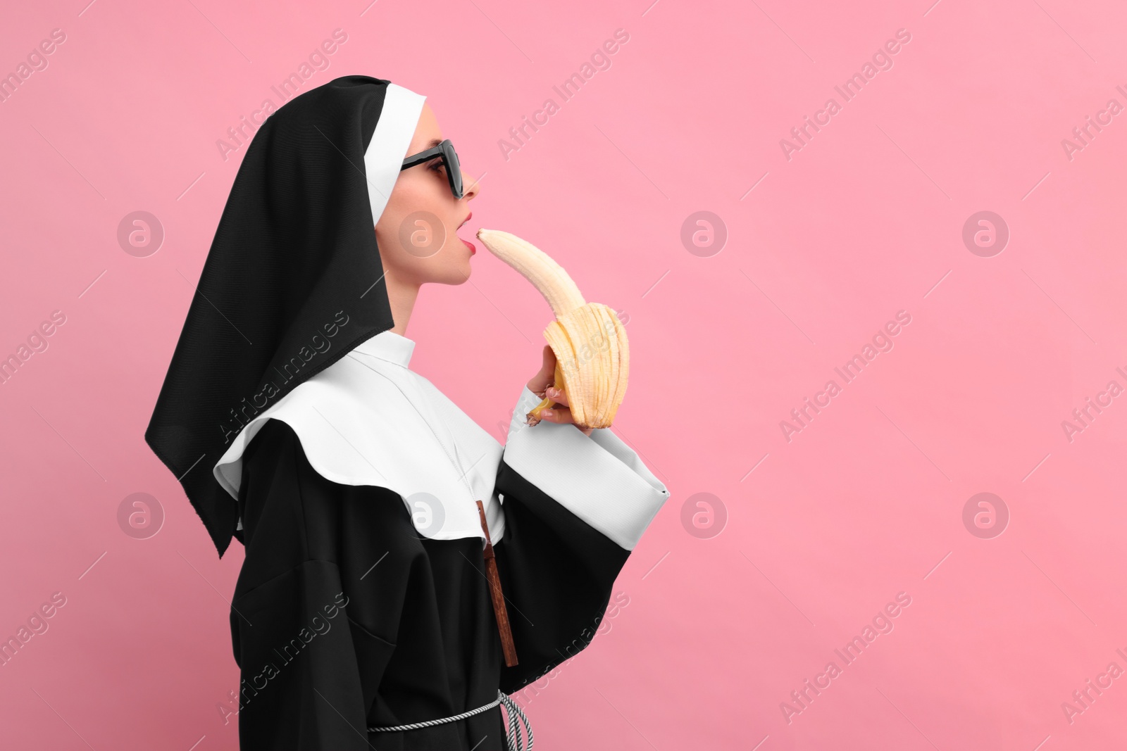 Photo of Woman in nun habit with banana against pink background, space for text. Sexy costume