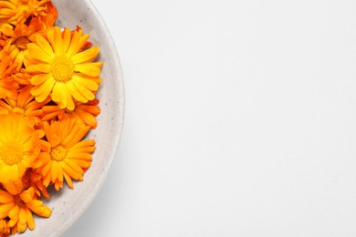 Beautiful fresh calendula flowers in bowl on beige background, top view. Space for text
