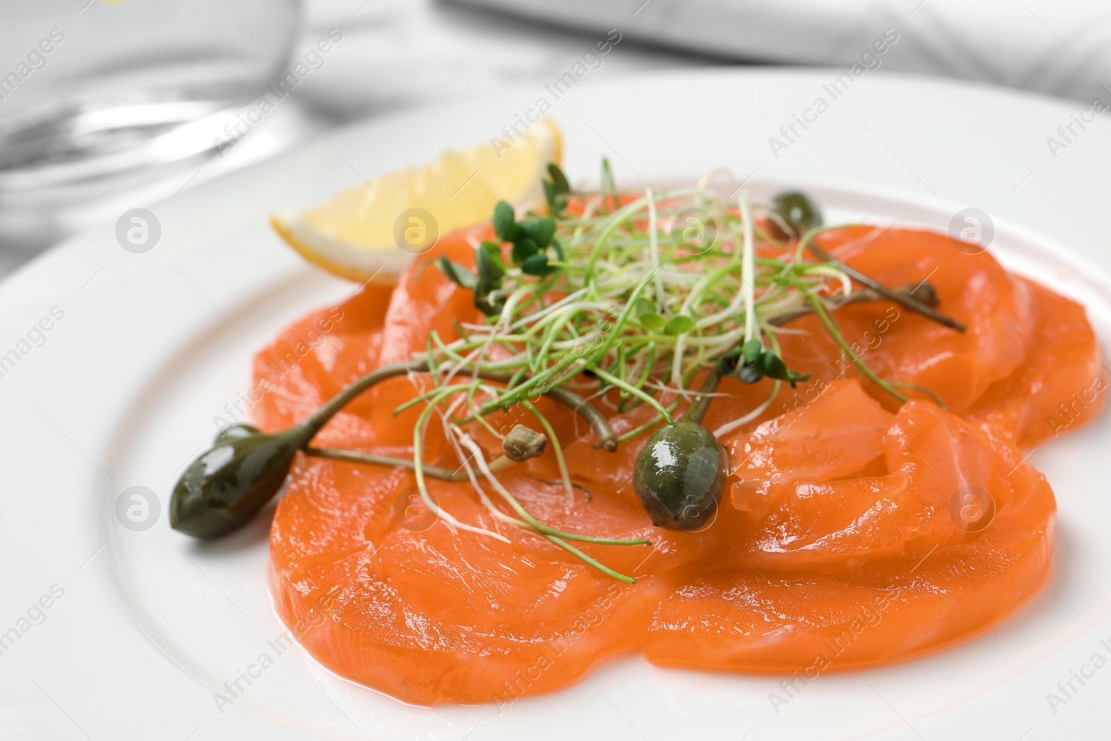 Photo of Salmon carpaccio with capers, microgreens and lemon on plate, closeup