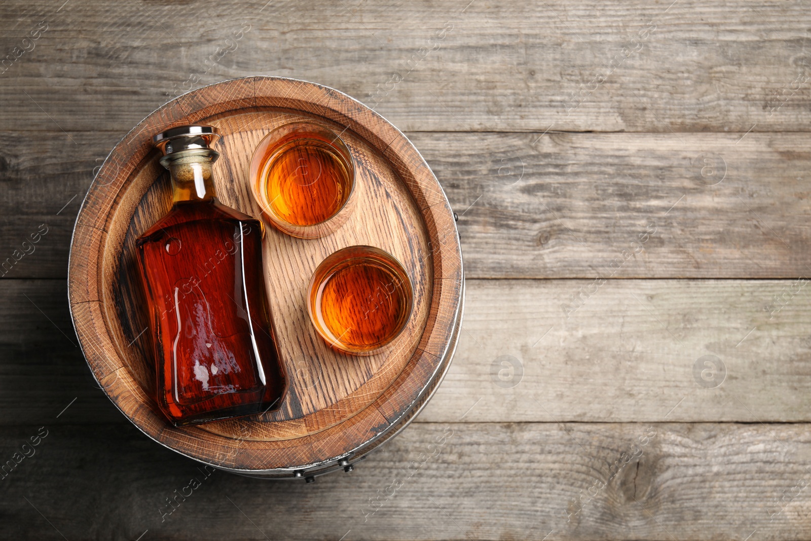 Photo of Glasses and bottle of whiskey with wooden barrel on table, top view. Space for text