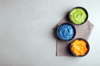 Photo of Bowls of different cream with food coloring on light table, flat lay. Space for text