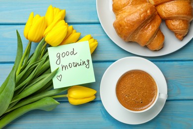 Photo of Cup of aromatic coffee with croissants, beautiful yellow tulips and Good Morning note on light blue wooden table, flat lay