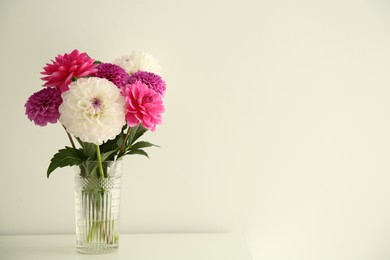 Photo of Bouquet of beautiful Dahlia flowers in vase on table near white wall, space for text