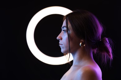 Photo of Beautiful woman and ring lamp on dark background in neon lights