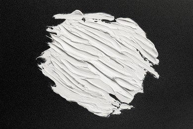 Photo of Strokes of white oil paint on black canvas, top view