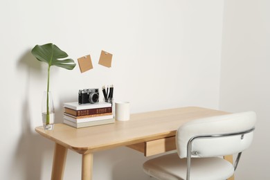 Comfortable workplace with wooden desk near white wall indoors