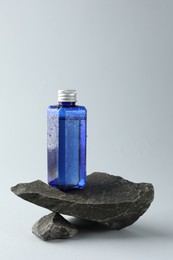 Bottle of cosmetic product on stones against light grey background