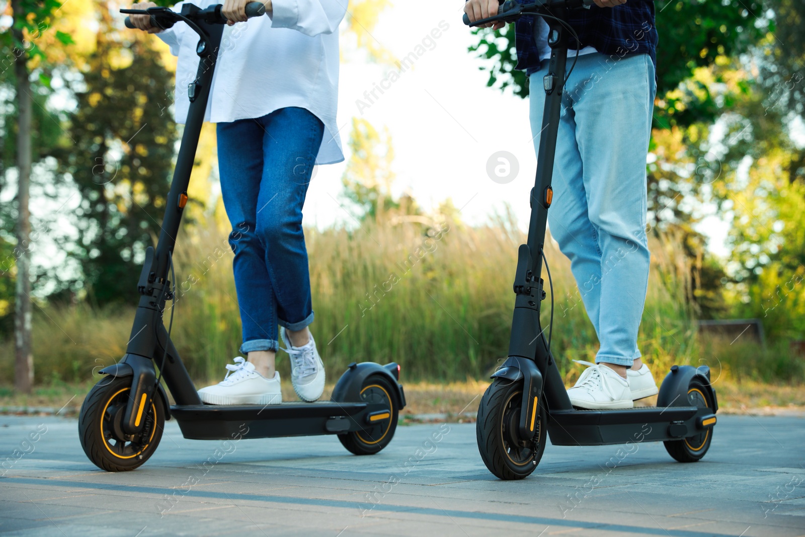 Photo of Couple riding modern electric kick scooters in park, closeup