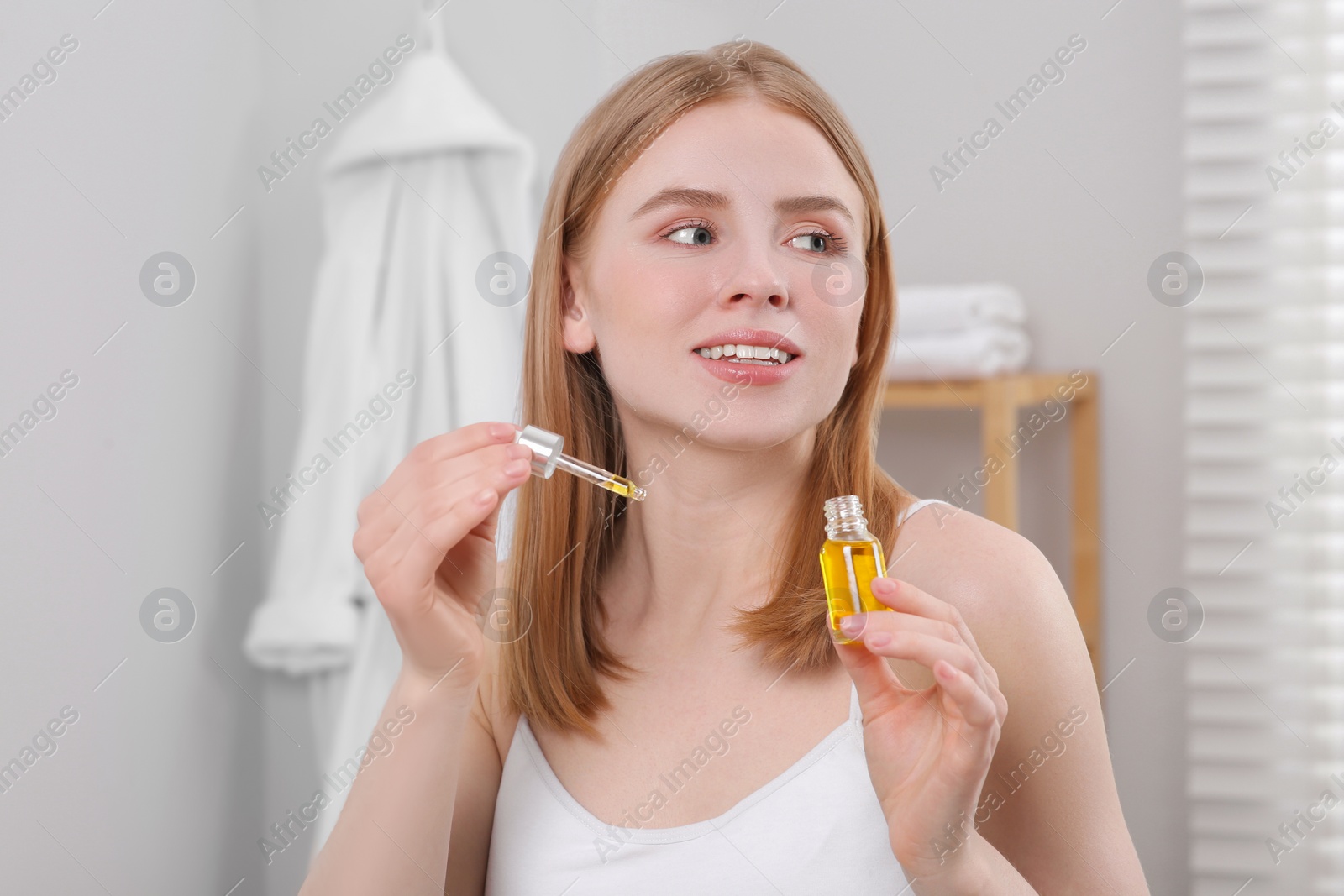 Photo of Young woman with bottle of essential oil in bathroom