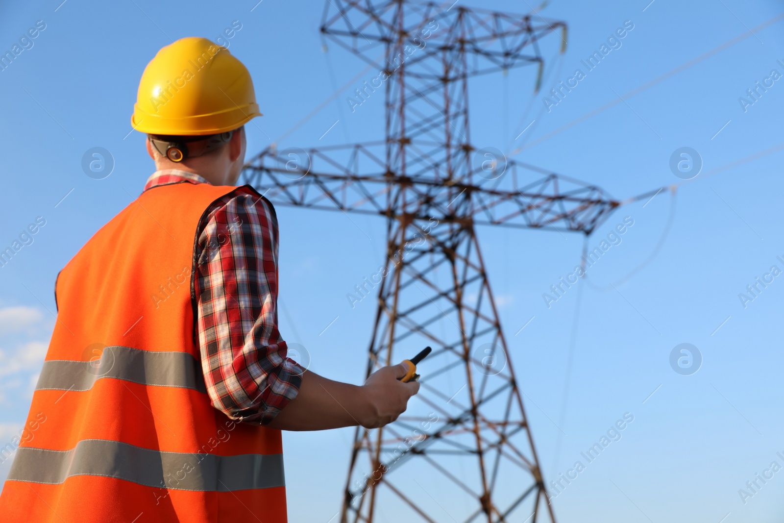 Photo of Electrical engineer with walkie talkie near high voltage tower