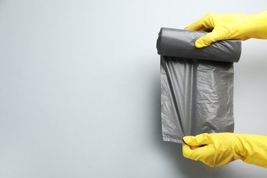 Photo of Janitor in rubber gloves holding roll of grey garbage bags over light background, top view. Space for text