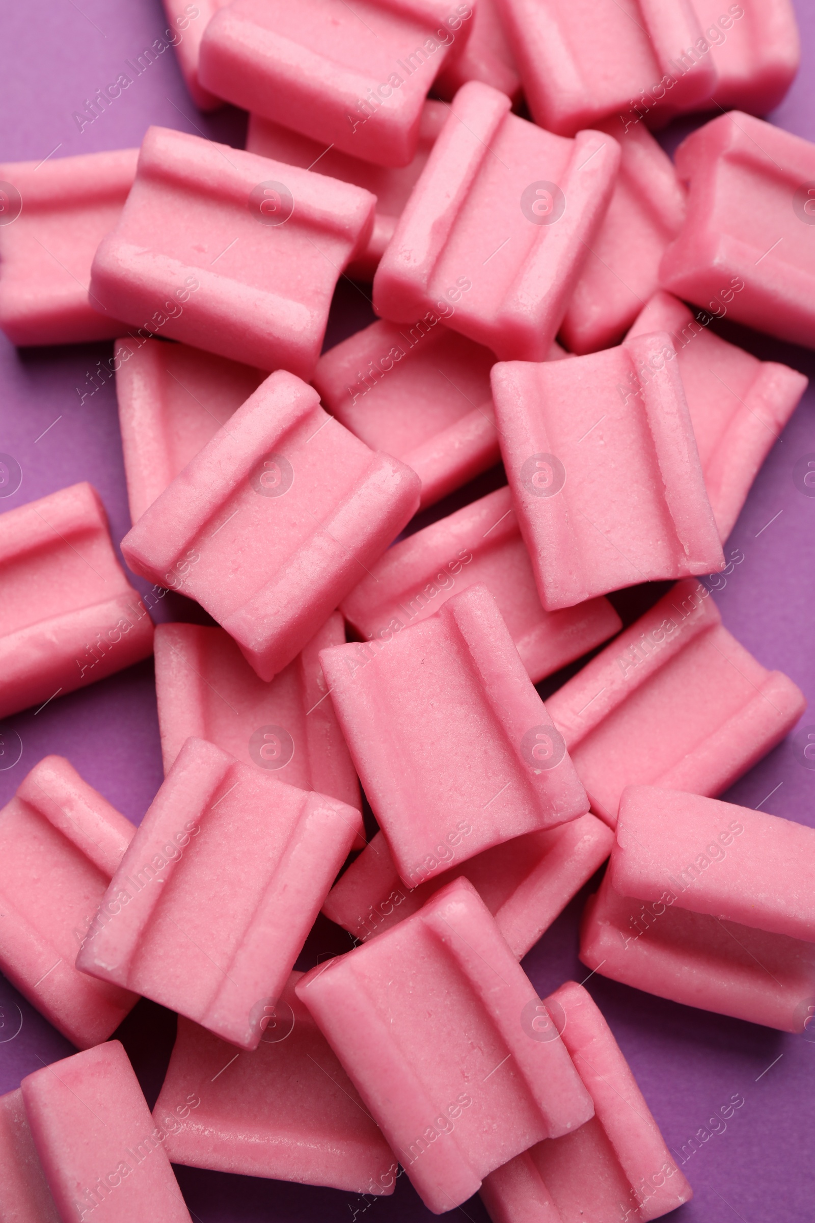 Photo of Tasty pink chewing gums on purple background, top view