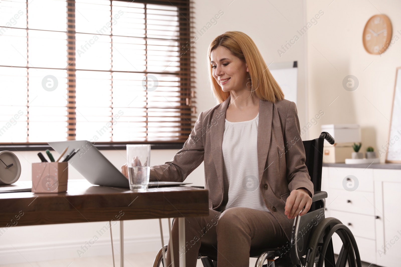 Photo of Portrait of woman in wheelchair working with laptop at table indoors