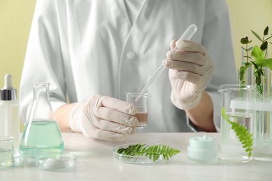 Scientist making cosmetic product at white table in laboratory, closeup