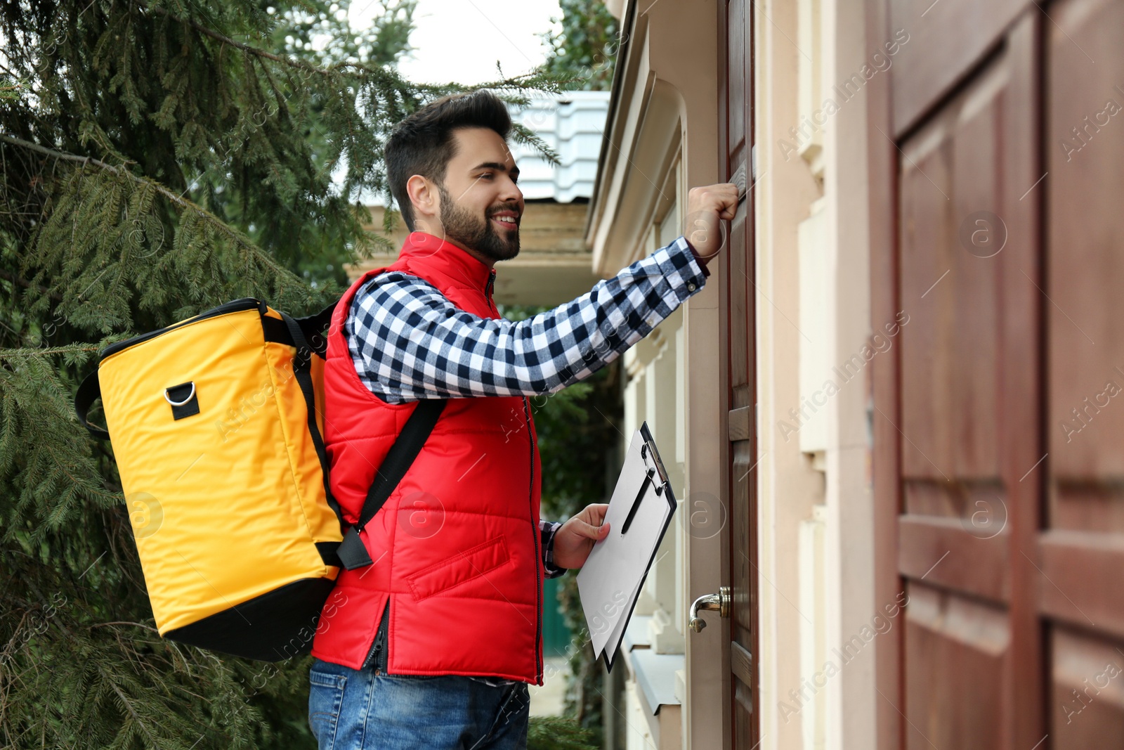 Photo of Courier with thermo bag and clipboard knocking on customer's house. Food delivery service