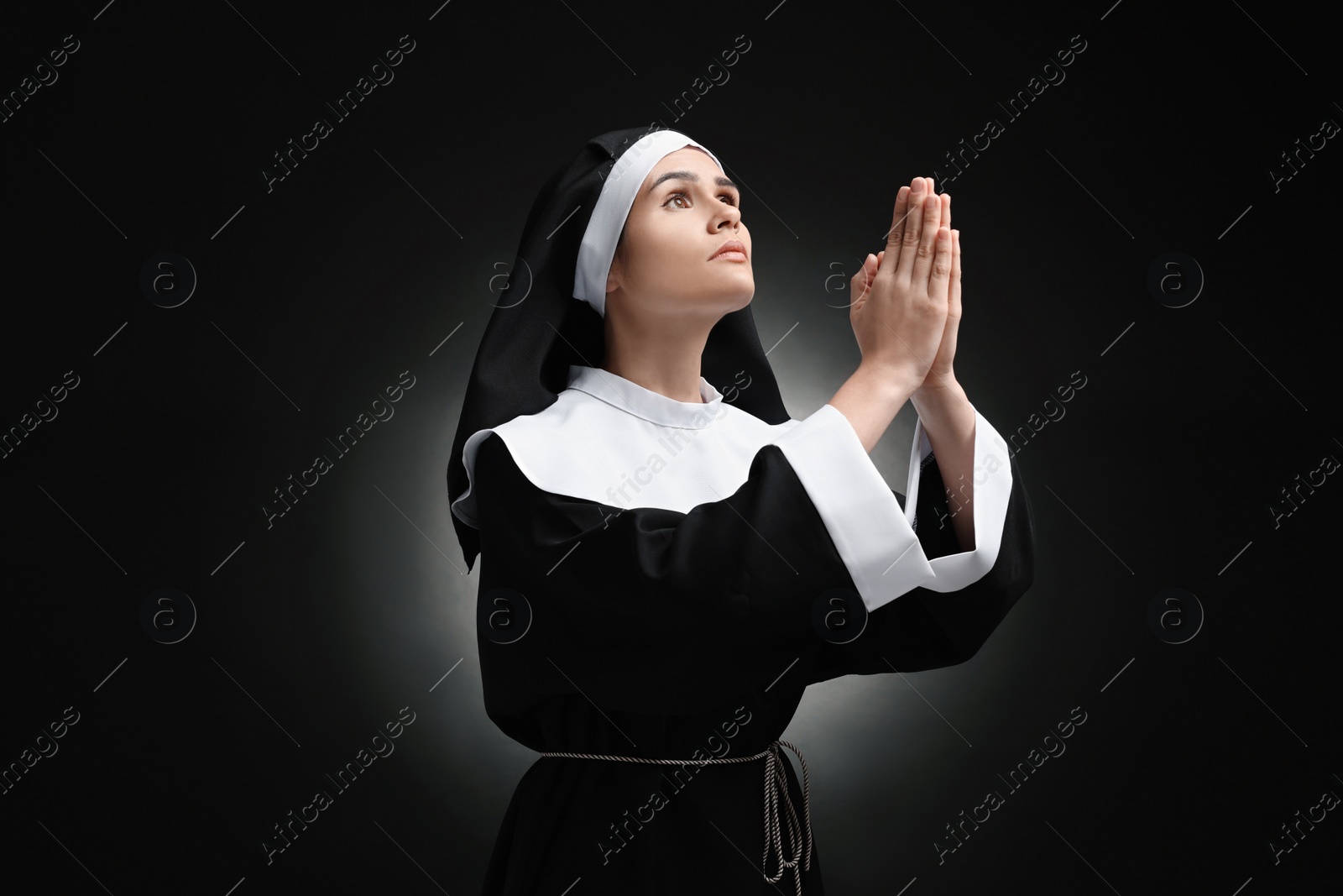 Photo of Nun with clasped hands praying to God on black background