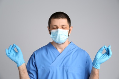 Photo of Doctor in protective mask meditating on grey background. Dealing with stress caused by COVID‑19 pandemic