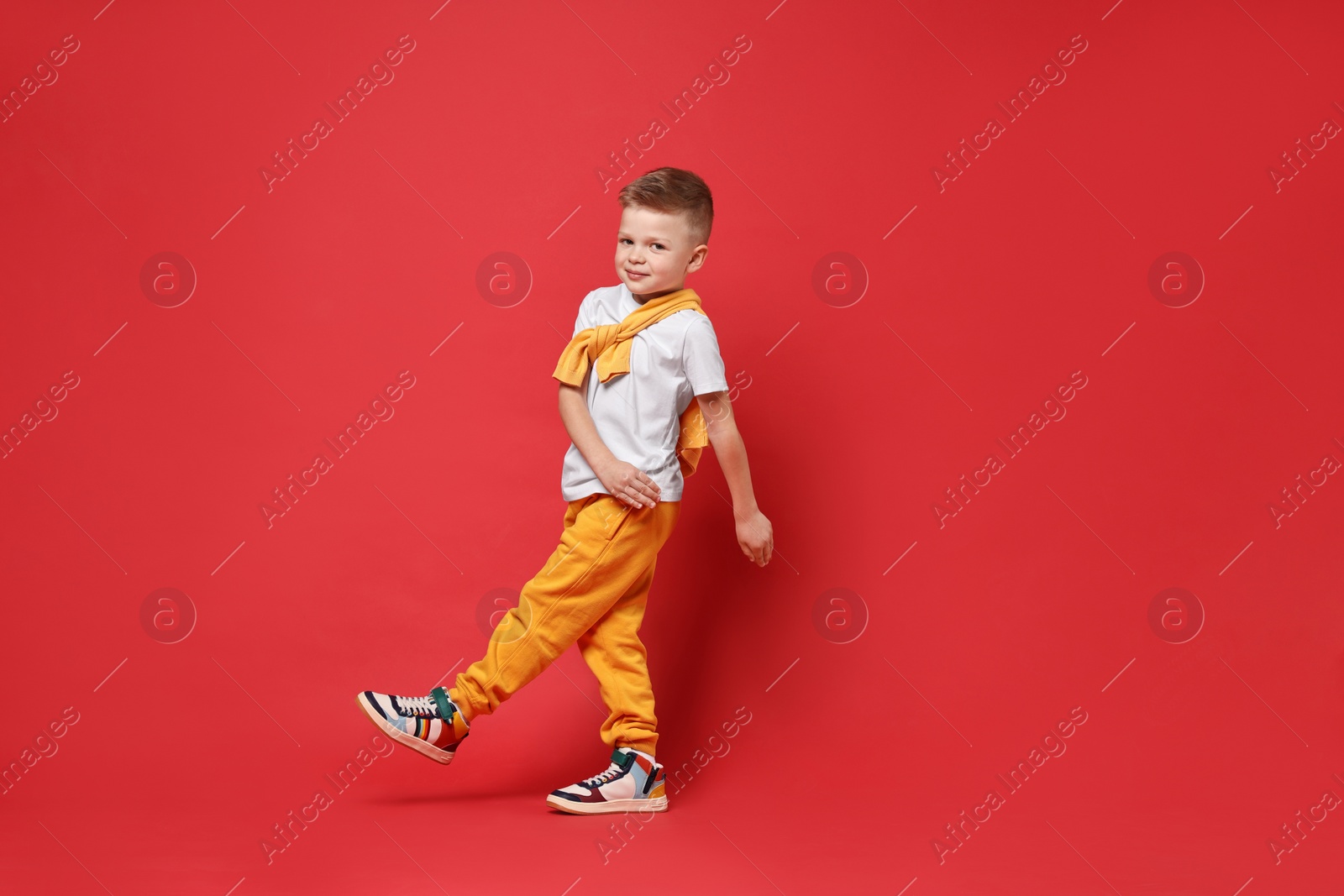 Photo of Happy little boy dancing on red background. Space for text