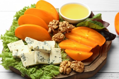 Photo of Delicious persimmon, blue cheese, nuts and honey served on white wooden table, closeup