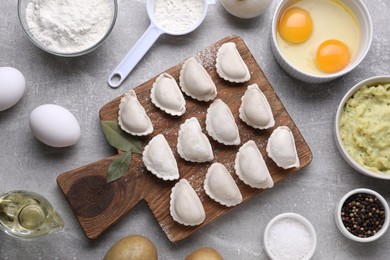 Raw dumplings (varenyky) and ingredients on grey table, flat lay