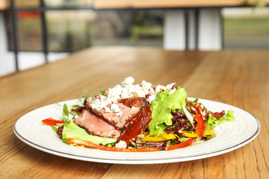 Photo of Delicious salad with roasted meat and vegetables served on wooden table indoors. Space for text