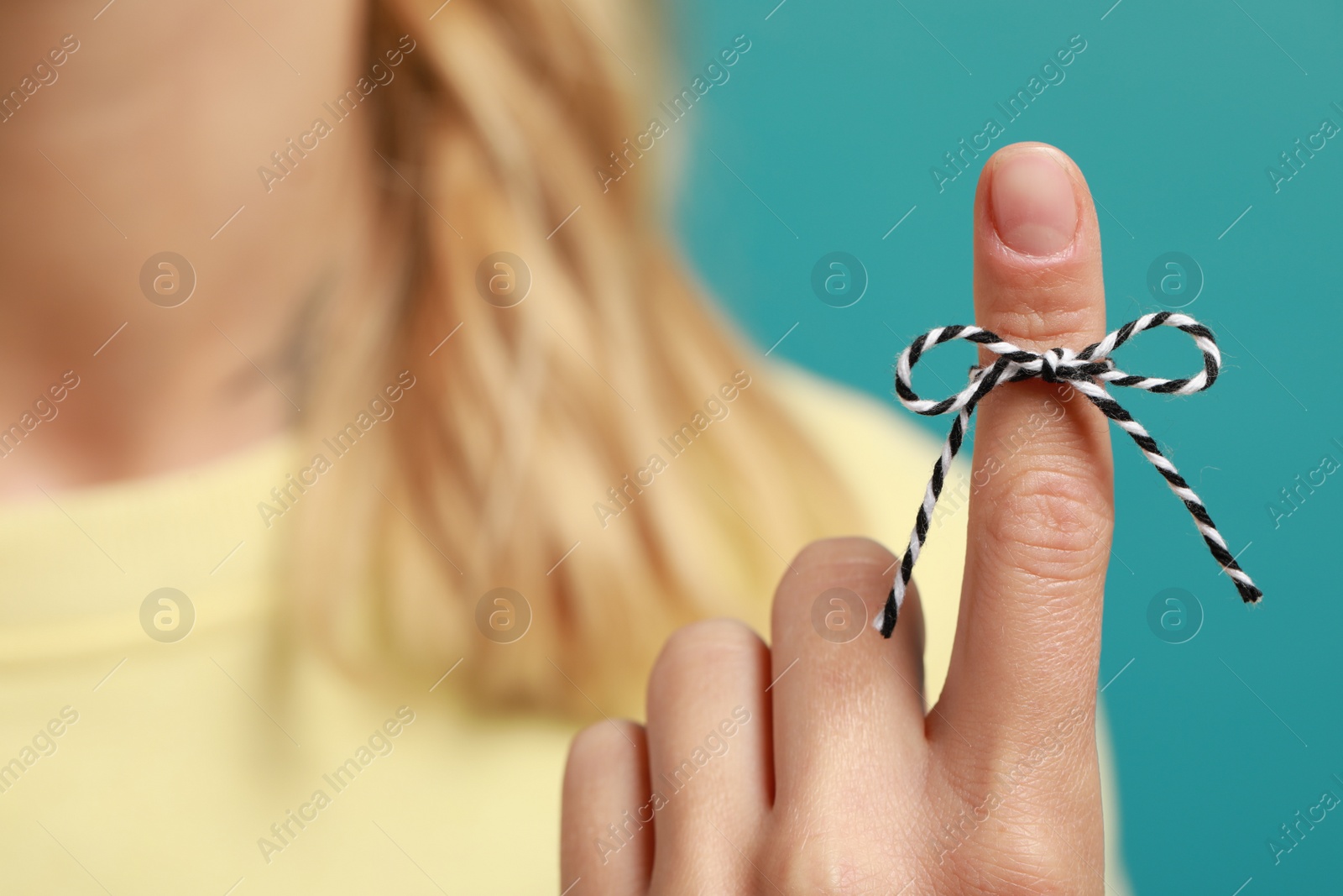 Photo of Woman showing index finger with tied bow as reminder against light blue background, focus on hand