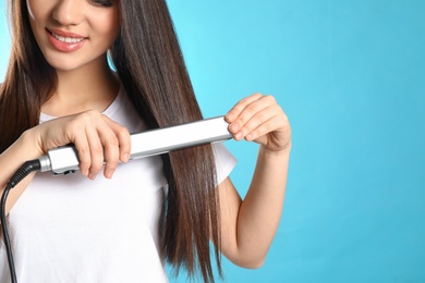 Photo of Happy woman using hair iron on color background, closeup. Space for text