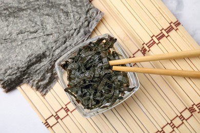 Photo of Chopped nori sheets with chopsticks on white marble table, top view