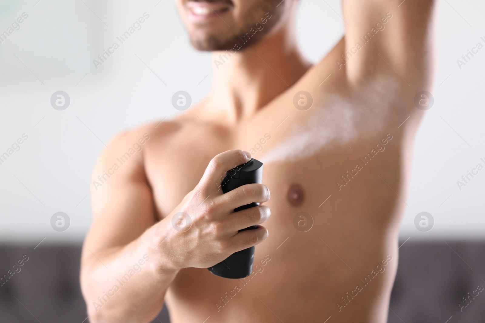 Photo of Handsome young man applying deodorant in room