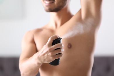 Photo of Handsome young man applying deodorant in room