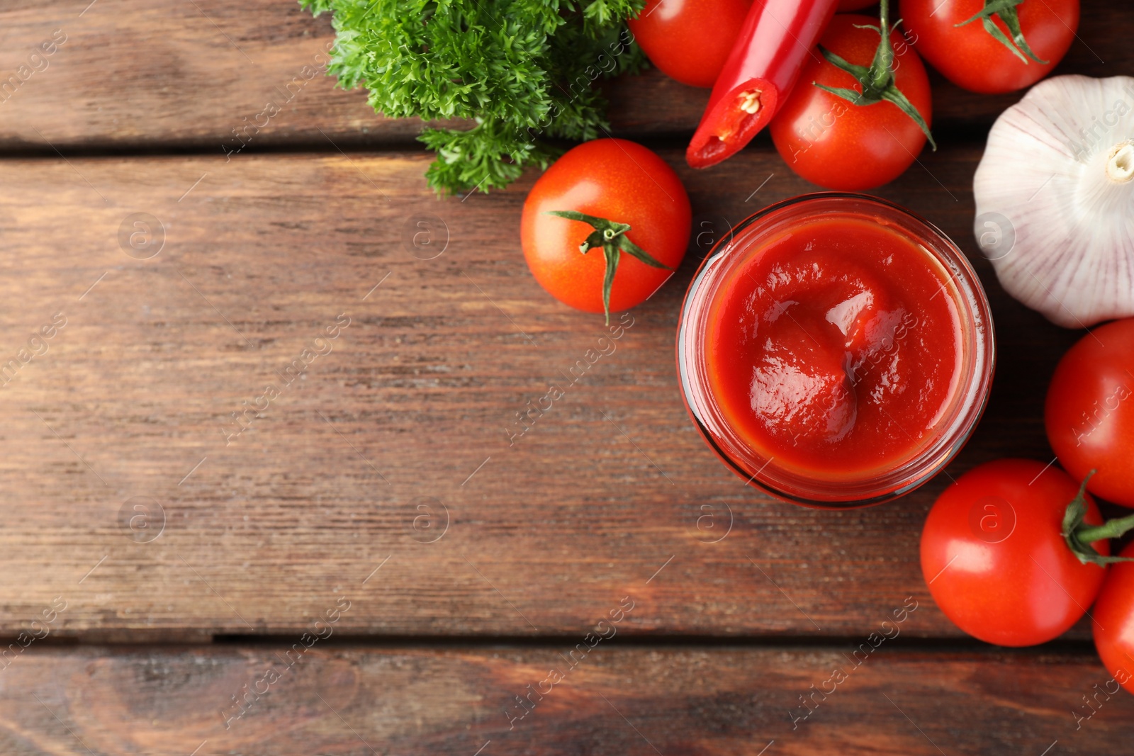 Photo of Jar of tasty ketchup and ingredients on wooden table, flat lay. Space for text