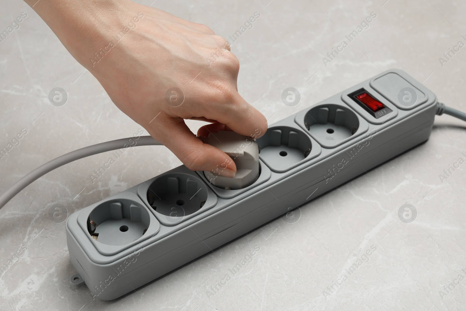 Photo of Woman putting plug into extension cord at grey marble table, closeup. Electrician's equipment