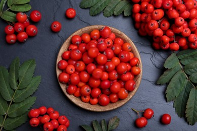 Photo of Fresh ripe rowan berries and leaves on black table, flat lay