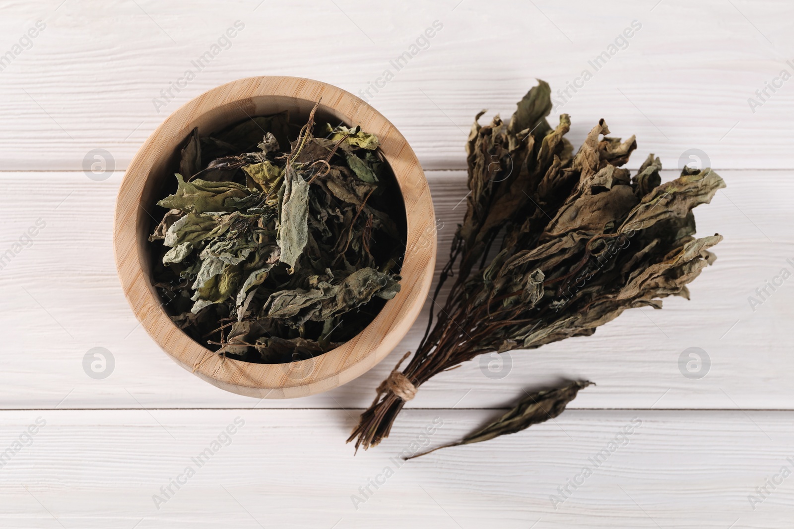 Photo of Bowl with dry basil on white wooden table, flat lay