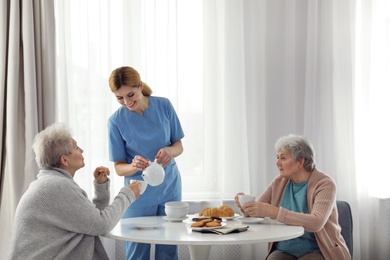 Photo of Nurse assisting while elderly women having breakfast at retirement home