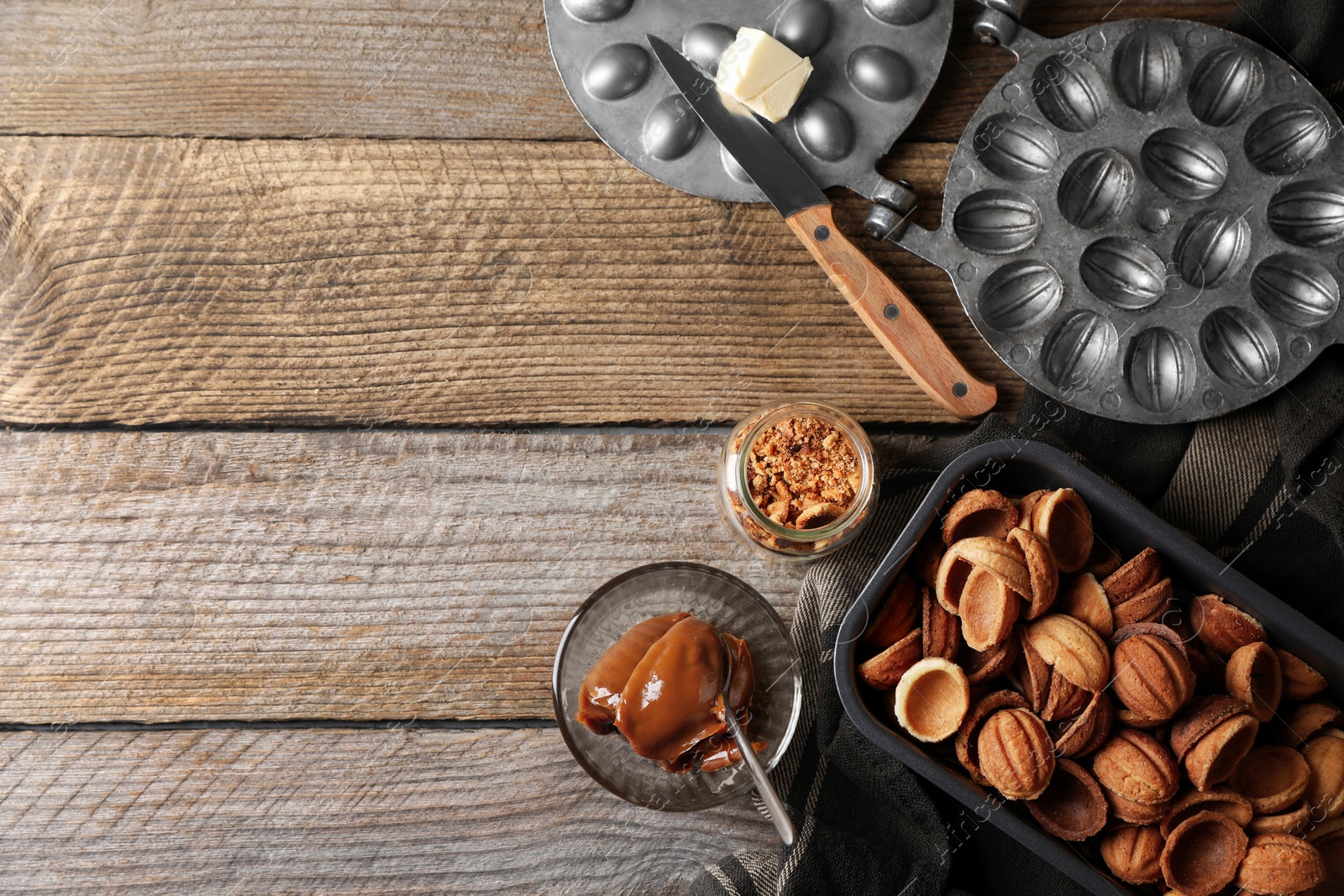 Photo of Making walnut shaped cookies. Cooked dough, mold, boiled condensed milk and nuts on wooden table, flat lay. Space for text