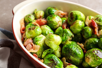 Delicious Brussels sprouts with bacon in baking dish on table, closeup