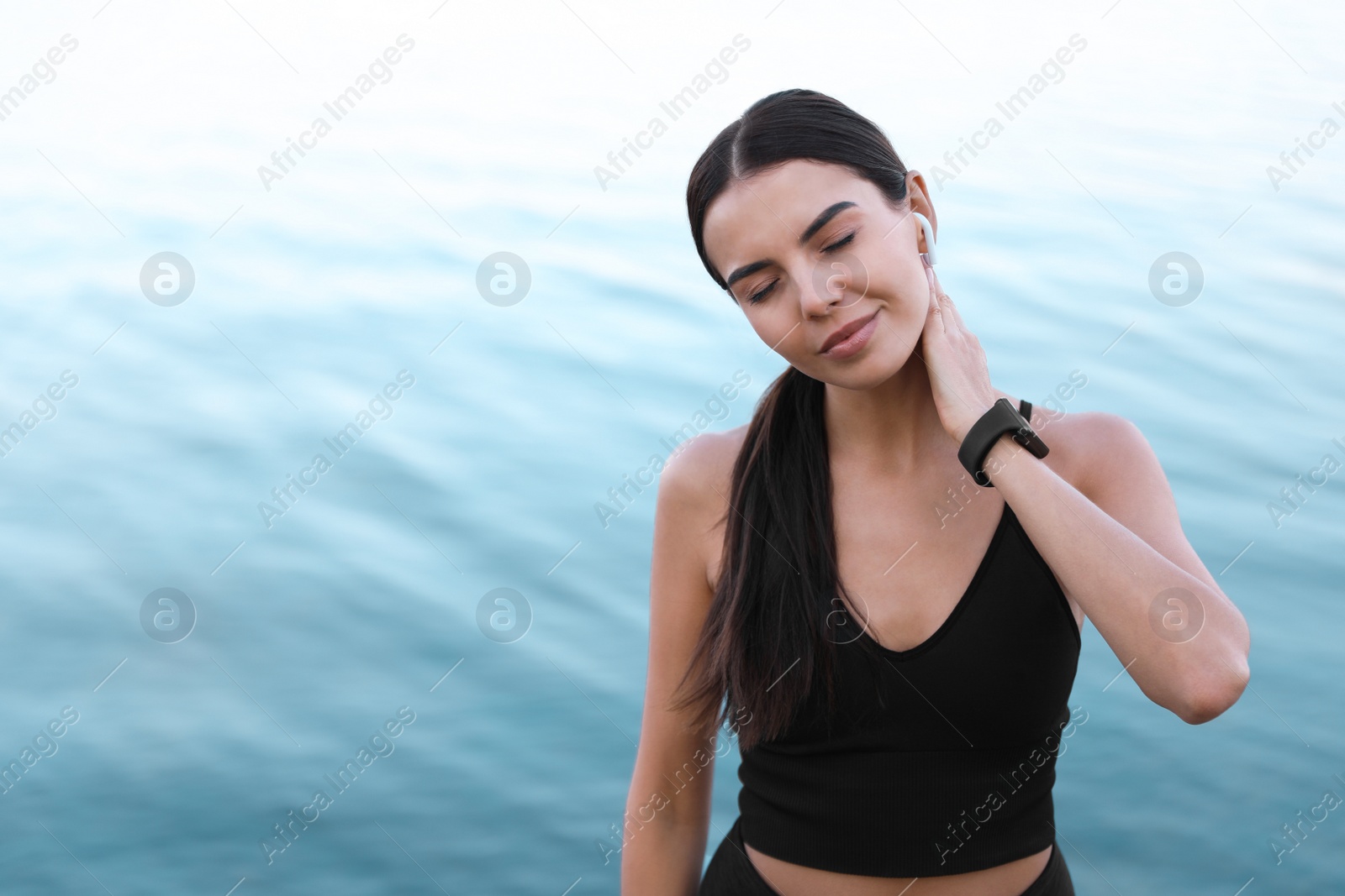 Photo of Young sportswoman with wireless earphones near river