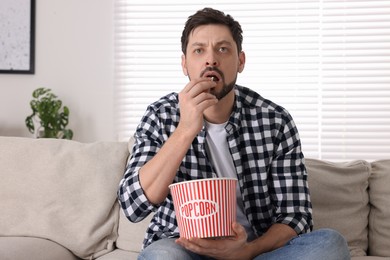 Photo of Man watching TV while eating popcorn on sofa at home